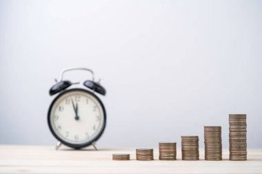 Tahta masa, zaman ve para yönetimi konsepti üzerinde alarm saati istiflenmiş madeni paralar.
