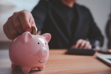 Elle kumbaraya para koymak para tasarrufu, mali planlama yönetimi ve finansal sorumluluk ve akıllı para alışkanlıklarını gösteren uzun vadeli yatırımları sembolize eder.