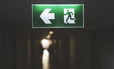 Modern bina koridorunda koşan adam simgesi ve okla yeşil çıkış işareti yangın çıkışı, acil çıkış, güvenlik işareti ve kamu güvenliğini temsil ediyor..