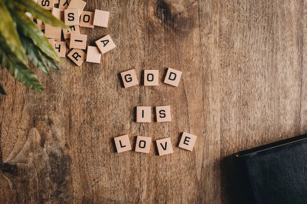 God is love spelled in block letters on a wooden table with a bible and a plant. Top view flat lay.