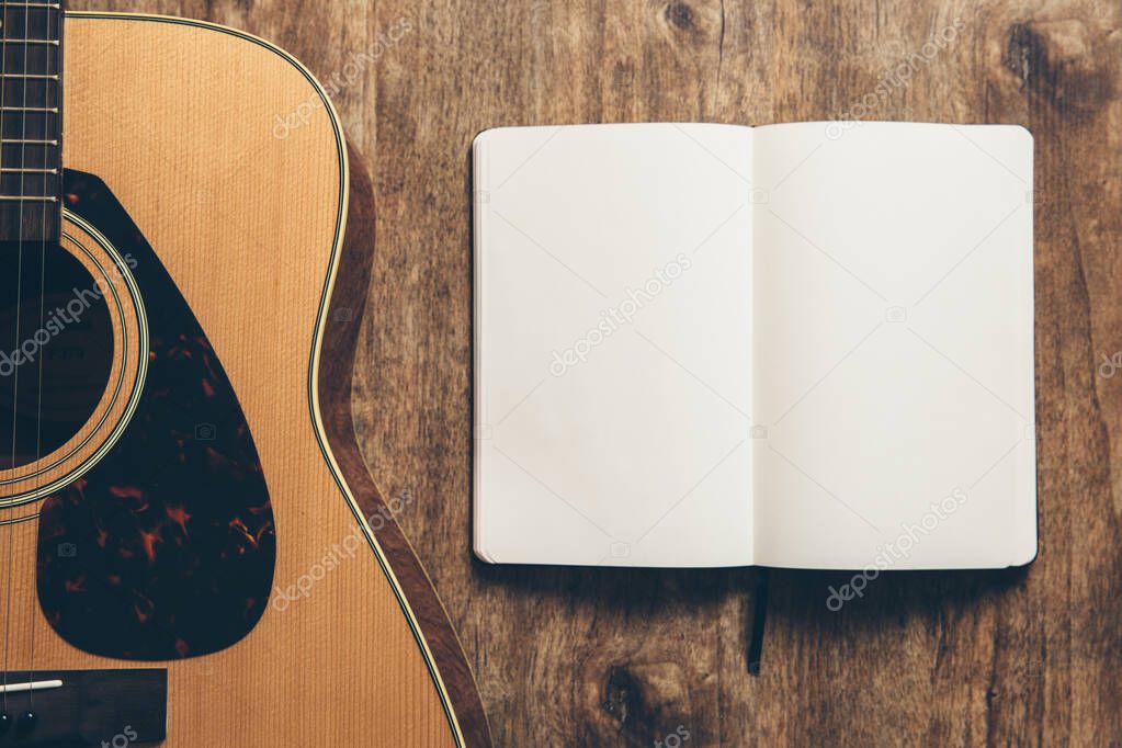 A guitar and a notebook on a wooden background.