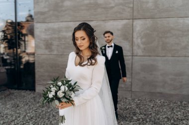 Gelin beyaz bir gelinlik giymiş ve elinde beyaz şakayık gülleri ve okaliptüs yapraklarından oluşan bir buket ile damadı bekliyor. Gelin ve damadın ilk buluşması.