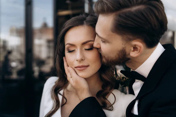 Damat güzel gelini yanağından öpüyor. Yeni evli şirin bir çiftin portresi. Erkek bir kadını öper.