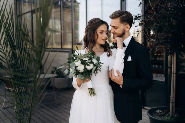 Damat geline sarılıyor. Palmiye yapraklarının yanında yeni evlenmiş sevimli Avrupalı bir kadının portresi. Düğün açık havada.