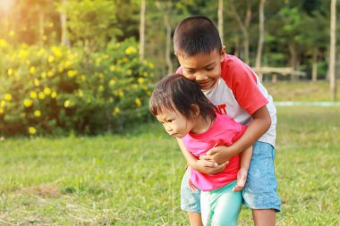 Mutlu Asyalı çocuklar gülümsüyor ve gülüyor. Küçük bir erkek kardeş, küçük kız kardeşine sarılıp oyun bahçesinde oynuyor. Aile kavramı.