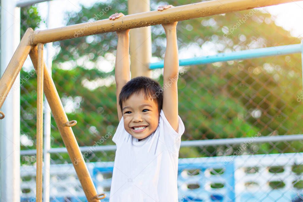 Kid exercise for health and sport concept. Happy Asian student child boy playing and hanging from a steel bar at the playground. 5-6 years old.