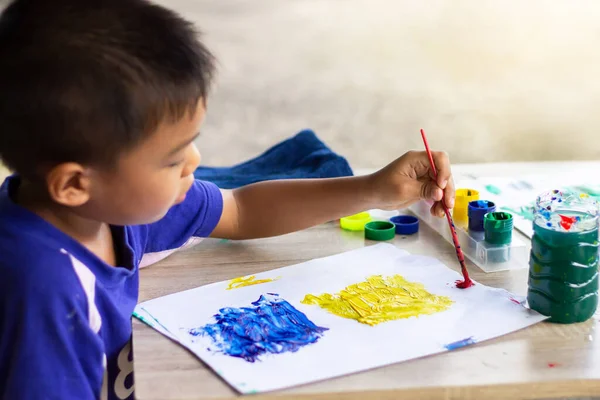 Portrait image of 5 yeas old child boy. Asian student drawing and painting colors on the paper in the classroom. Kid and education concept