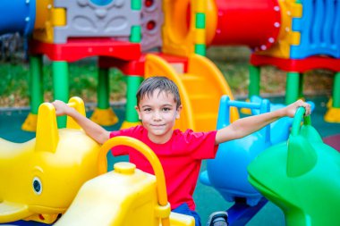 Kırmızı tişörtlü mutlu bir çocuk lunaparkta eğleniyor. Mutlu bir çocuğun portresi