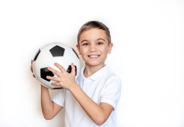 Elinde futbol topu tutan duygusal bir çocuğun portresi. Beyaz arka planda beyaz tişörtlü bir çocuk. Kameraya bakıyorum. Metin için yer. 