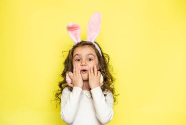 Mutlu ve sürpriz bir gülümsemesi olan neşeli bir kız yanaklarına dokunur ve Paskalya yumurtalarını elinde tutar, sana olan aşkını ifade eder, tüylü kulaklar giyer, tişört giyer. Mutlu anlar. Paskalya ve tatil konsepti 