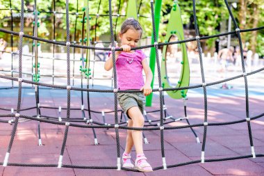 Küçük neşeli kız oyun parkındaki parkta tatilde oynuyor. Çocuk tatilde caddede eğleniyor. Çocuk simülatörlerle spor yapıyor.. 