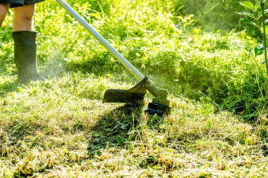 Şehir parkında ya da arka bahçede elektrikli çim biçme makinesiyle çim biçen bir işçi. Bahçıvanlık malzemeleri ve ekipmanlar. Çim biçme makinesiyle çim biçme işlemi