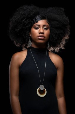 Siyah elbiseli Afrikalı bir model. Siyah arka planda büyük afro saçı var.