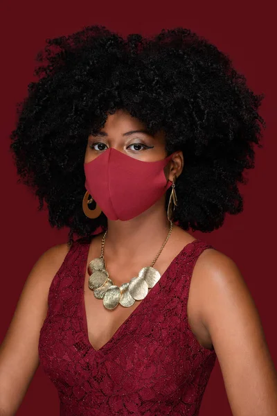 young black woman wearing red mask and protection against covid-19 during christmas party isolated on red background