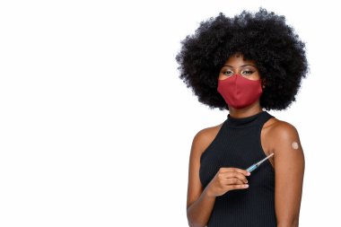Yüzünde bir gülümseme ile Covid-19 'a karşı koruyucu maske takan siyah bir genç beyaz arka planda izole edilmiş aşı markasını gösteriyor.