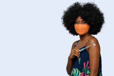  Siyah genç, Covid-19 'a karşı koruyucu maske takıyor. Yüzünde bir gülümsemeyle aşının markasını gösteriyor. 