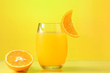 Portakal suyu bardağı, portakalın yarısı sarı arka planda yalıtılmış.