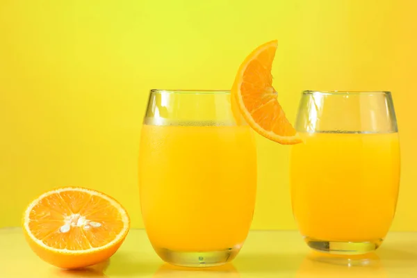 glass with orange juice, half of an orange next to the glass insulated in yellow background