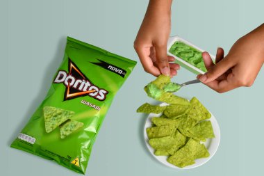 SO PAULO, BRAZIL - JULY 13, 2021HANDS HOLDING SALTY SNACKS WHILE PUTTING SAUCE ON THEM, PACKAGE OF DORITOS WASABI 