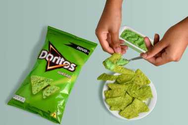 SO PAULO, BRAZIL - JULY 13, 2021HANDS HOLDING SALTY SNACKS WHILE PUTTING SAUCE ON THEM, PACKAGE OF DORITOS WASABI 