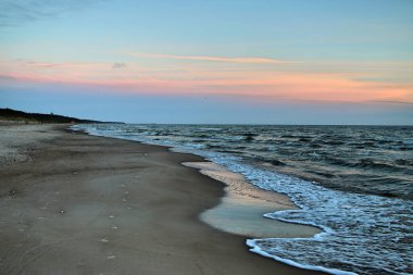 Gün batımında Baltık Denizi 'nde boş bir sahil. Dalgalar kuma dökülüyor. Mavi-pembe gökyüzü 