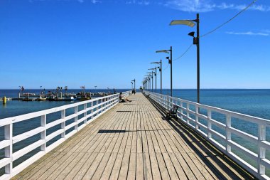 Güneşli bir günde Mechelinki 'de Baltık Denizi' ndeki ahşap iskele. Bulutsuz mavi gökyüzü. Arka planda, mavi deniz ve mekanik balıkçıların limanı. Haziran 2021, Mechelinki, Polonya