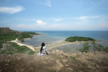Genç bir gezgin kız Balanan Sahili 'nde bir tepenin kenarında oturuyor ve Baluran Ulusal Parkı' nın güzel deniz manzarasının tadını çıkarıyor. Genç kızlar vahşi hayatı, gezmeyi, özgürlüğü severler..