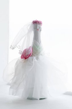 Gelinin elbisesiyle süslenmiş bir şampanya şişesi pencere eşiğinde duruyor. Düğün kompozisyonu