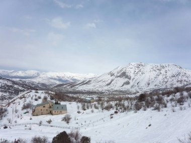 Karlı Chimgan Dağları, kışın dağların arasında yalnız bir ev duruyor.