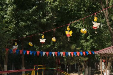 Kelebekler ve arılar plastik şişelerden ve renkli bayraklardan oluşur. Bir halata tutunup çocuk parkının arka bahçesindeki ağaçlara asılırlar.