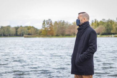 Maskeli bir adam gölün kenarındaki parkta duruyor.