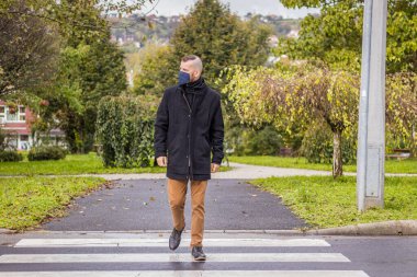 Bir adam damlayan yağmurda Macaristan 'ın küçük bir şehrinde maske takarak yürür.