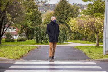 Bir adam damlayan yağmurda Macaristan 'ın küçük bir şehrinde maske takarak yürür.