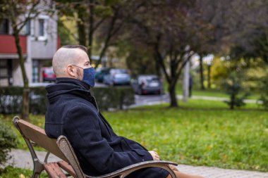 Yerel parktaki damlayan yağmurda bir adam kırık bir bankta oturuyor.