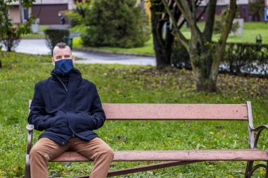 Yerel parktaki damlayan yağmurda bir adam kırık bir bankta oturuyor.