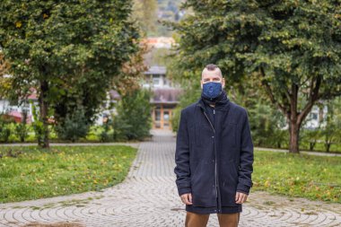 Damlayan yağmurda, Macaristan 'da maske takan bir adam küçük bir parkta duruyor.