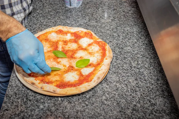 Bir adam yerel bir pizza ve jiroskop restoranında margherita pizza yapıyor.