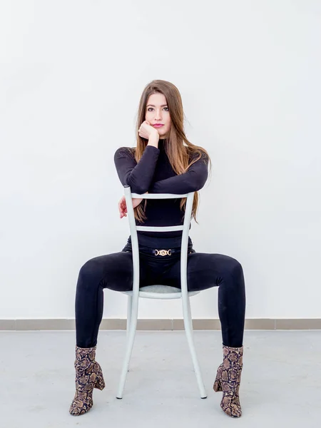 Beautiful young woman sitting on a chair over white wall