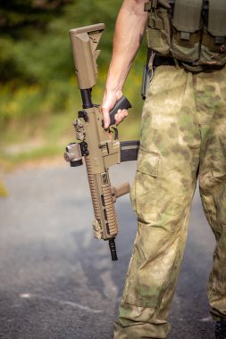 Askeri üniformalı, yumuşak bir saldırı tüfeği tutan bir adama yaklaş.