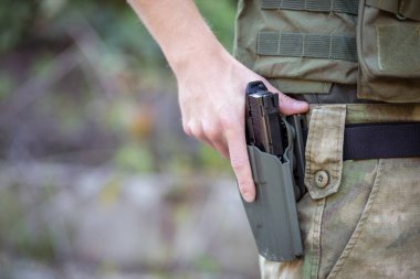 Askeri üniformalı, yumuşak bir tabanca tutan bir adama yaklaş.