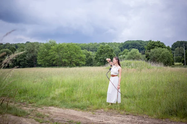 A Hungarian woman standing on the field in a linen dress with a whip