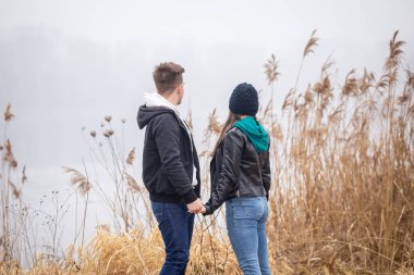 Sisli bir kış gününde gölün kenarında duran genç çift