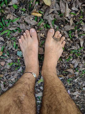 Bir adamın çıplak ayaklarını kuru yapraklar ve otların arasında yakalayıp doğa ve özgürlükle bir bağ kurmasını sağlayan bir görüntü..