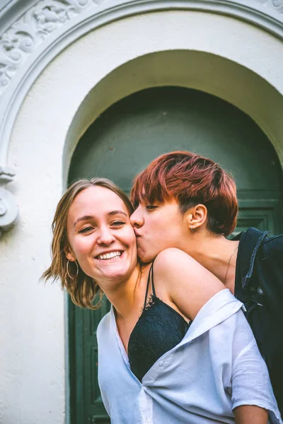 Girls couple standing kissing in a dark green door on the street.