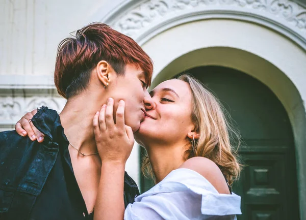 Girls couple standing kissing in a dark green door on the street.