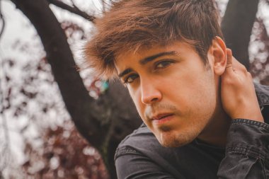 Elleri ensesinde, sonbahar günü parkta kameraya bakan bir adam.. 