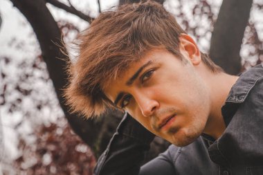 Elleri ensesinde, sonbahar günü parkta kameraya bakan bir adam.. 