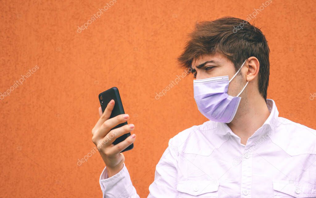 Guy with purple face mask looking at his smartphone on a orange background.