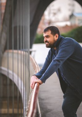 Olgun sakallı adam gülümsüyor, gün batımında Madrid Köprüsü 'nün korkuluklarına yaslanıyor..