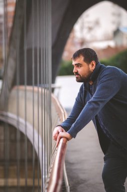 Olgun sakallı adam gün batımında Madrid Köprüsü 'nün korkuluklarına yaslanıyor..